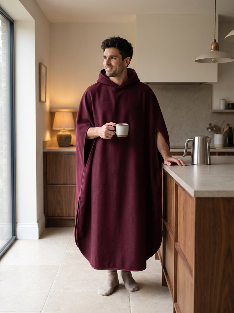 A man in a Wine Enfold holding a mug in a warm walnut kitchen, with his forearms free through the open sides.